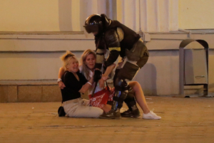 A Belarusian law enforcement officer approaches women, who react while sitting on the pavement during a rally of opposition supporters following the presidential election in Minsk, Belarus August 10, 2020. The opposition rejected official election results handing President Alexander Lukashenko a landslide re-election victory.