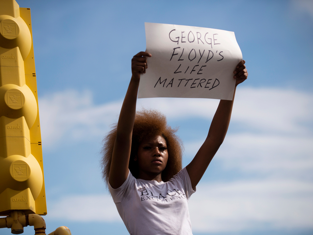	MINNEAPOLIS, MN - MAY 26: A woman holds a sign stating "George Floyd's Life Mattered" during a protest outside the Cup Foods on May 26, 2020 in Minneapolis, Minnesota. Four Minneapolis police officers have been fired after a video taken by a bystander was posted on social media showing Floyd's neck being pinned to the ground by an officer as he repeatedly said, "I canâ€™t breathe". Floyd was later pronounced dead while in police custody after being transported to Hennepin County Medical Center.