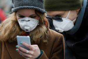 People wearing protective face masks use a smartphone on a street amid coronavirus (COVID-19) concerns in Kiev, Ukraine March 17, 2020.