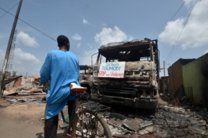 A cyclist reads a sign on a burnt truck calling for violence to stop in the market of Toumodi on November 4, 2020, during a campaign of non-violence and peace awareness by young volunteers after inter-community clashes during the country's presidential election of October 31, 2020. - Ivory Coast is caught in a standoff after Ivorian President Alassane Ouattara won a third term by a landslide in October 31, 2020's vote, which was boycotted by the opposition claiming an "electoral coup" in a nation with a constitutional two-term presidential limit. (Photo by SIA KAMBOU / AFP)