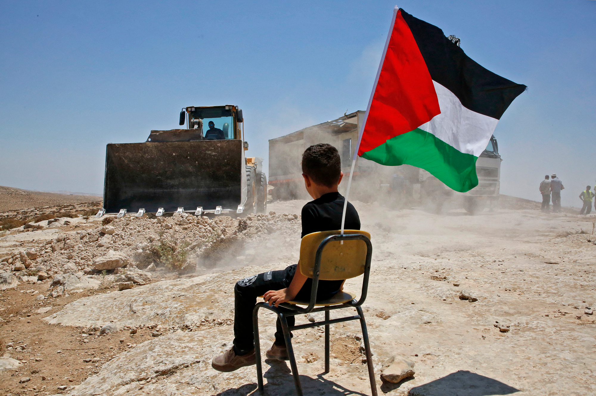 Un garçon palestinien est assis sur une chaise avec un drapeau national alors que les autorités israéliennes démolissent le site d'une école dans le village de Yatta, au sud de la ville d'Hébron en Cisjordanie, et pour être relocalisé dans une autre zone, le 11 juillet 2018.