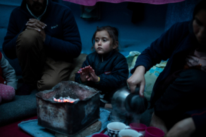Marjan Hosini, 3, warms her hands over hot coal as Yasamin, 25, Hosini's mother, pours tea into cups inside their temporary shelter at a makeshift camp for refugees and migrants next to the Moria camp, on the island of Lesbos, Greece, February 16, 2020. REUTERS/Alkis Konstantinidis
