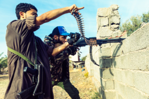 Sur la ligne de front de Al Swani pendant les affrontements, un combattant de la brigade 610 (GAN) tire avec sa mitraille alors que son camarade pointe du doigt l'ennemi. Depuis avril, l'armee nationale Libyenne (LNA) dirigee par Khalifa Haftar essaie de prendre le controôe de Tripoli defendu par les forces du gouvernement d'accord national de Fayez al-Sarraj, soutenu par l'onu (GAN). Libye, banlieue de Tripoli, 6 decembre 2019.