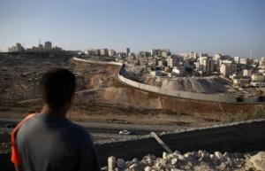 A picture taken on October 18, 2016 from the east Jerusalem Arab neighbourhood of Issawiya shows a Palestinian youth looking on as the Palestinian Shuafat refugee camp (R) is seen behind the controversial Israeli separation wall. (Photo by AHMAD GHARABLI / AFP)