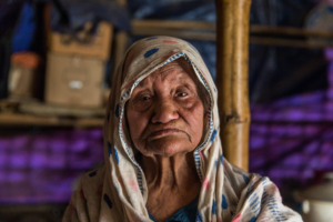 Sokhina Khatun, a Rohingya woman around 90 years old, stands for a portrait in her shelter in Camp #1 East (Kutupalong Camp), Bangladesh, 19 February 2019.

“I’ve fled [from Myanmar] four times in my life," she told Amnesty International. "The fourth time was in 2017. I came here with only my walking stick [and] this thami (longyi)… There has never been peace for us. We’ve had to flee here frequently. We were under persecution for so long.”

“My number one problem [in the camp] is the latrine. The latrine is down at the bottom [of the hill], it’s very difficult for me to go down there. Sometimes I just go inside [my shelter in a pan]… I’ve been surviving like that.”
