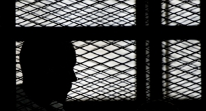 Al-Jazeera channel's Australian journalist Peter Greste stands inside the defendants cage during his trial for allegedly supporting the Muslim Brotherhood on June 1, 2014 at the police institute near Cairo's Tora prison. The high-profile case that sparked a global outcry over muzzling of the press is seen as a test of the military-installed government's tolerance of independent media, with activists fearing a return to autocracy three years after the Arab Spring uprising that toppled Hosni Mubarak. AFP PHOTO / KHALED DESOUKI (Photo credit should read KHALED DESOUKI/AFP via Getty Images)