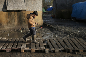 Un enfant migrant se fraie un chemin devant des abris dans un champ boueux appelé la jungle de Grande-Synthe, près de Dunkerque, dans le nord de la France, le 12 janvier 2016.