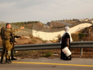 A Palestinian woman stands with others (not pictured) as they gather near an Israeli army checkpoint as they wait to reach their olives fields on the other side of Israel's separation barrier (background) after they received an special Israeli permission to harvest their olive trees, on October 13, 2021 near Bait A'wa village on the outskirts of the West Bank city of Hebron. (Photo by HAZEM BADER / AFP) (Photo by HAZEM BADER/AFP via Getty Images)