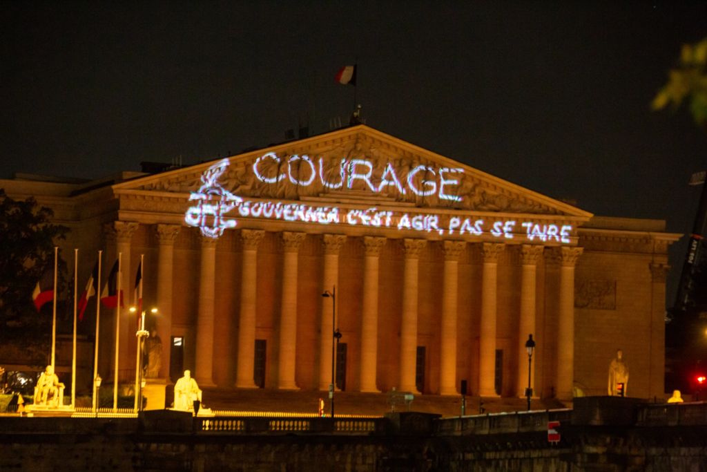 Projection "Courage : gouverner c'est agir, pas se taire" sur la façade de l'Assemblée nationale, à Paris, par Amnesty International le 21 avril 2026. Photo par Michael Bunel